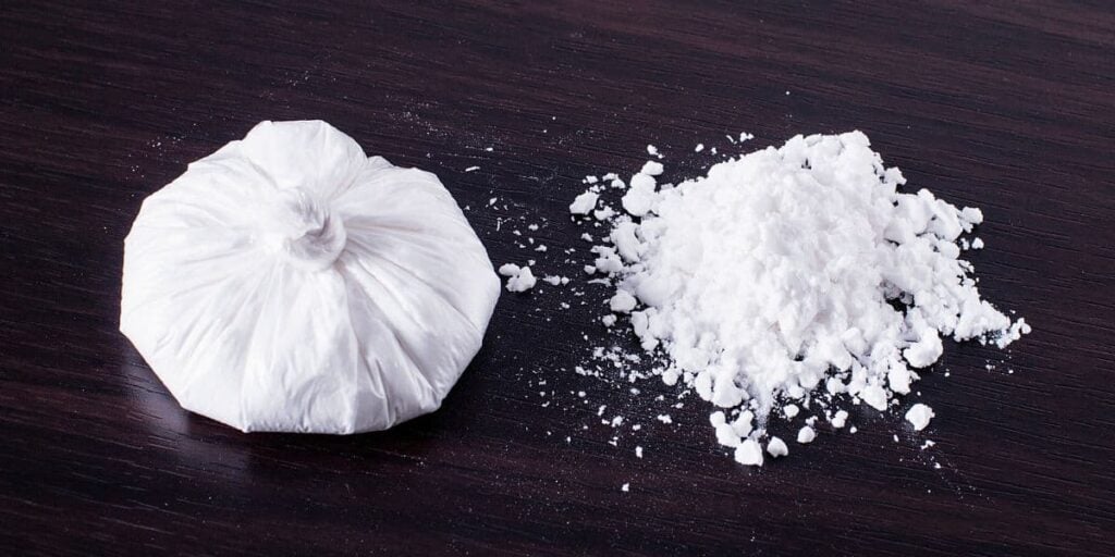 An assortment of cocaine products, including powder and an 8 ball, displayed in a blurred background.