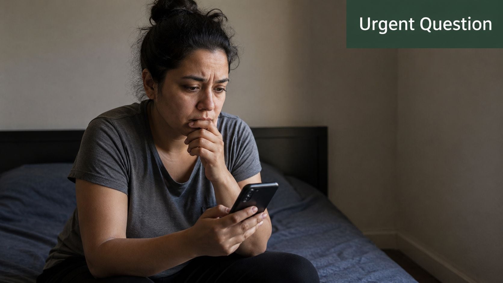 A concerned woman sitting on a bed looking at her smartphone with a worried expression.