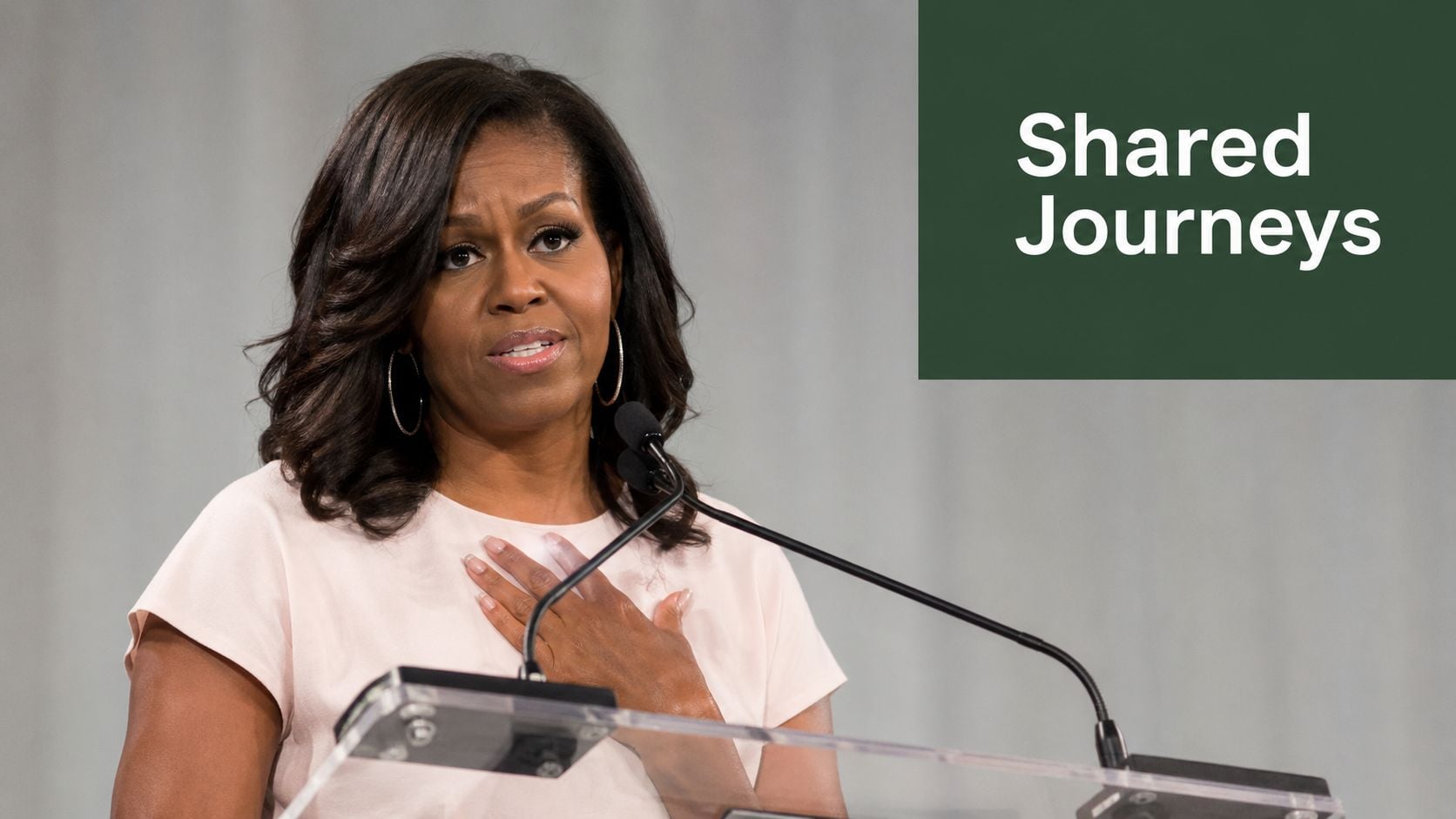 Former First Lady Michelle Obama speaking at a podium with the text Shared Journeys visible nearby.