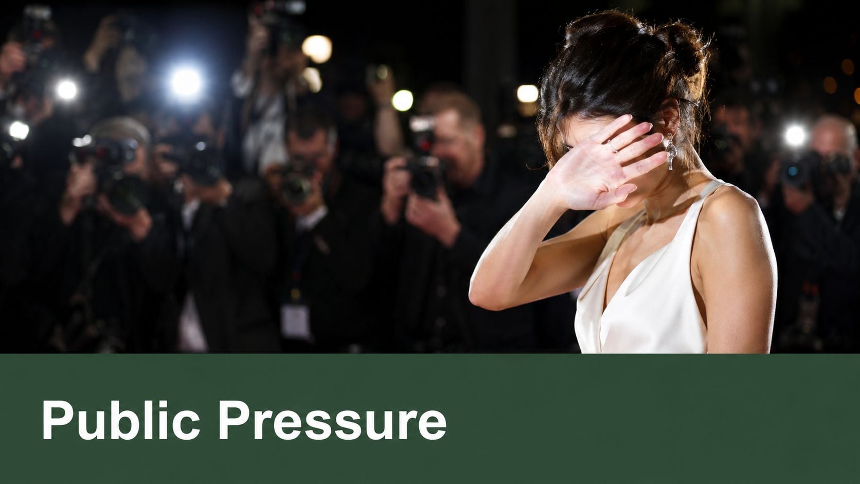 A celebrity shielding her face from multiple cameras and bright flashes while attending a red carpet event.