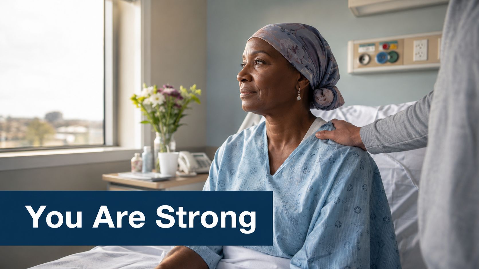 A caring individual supports a patient wearing a headscarf in a hospital room with the text You Are Strong.